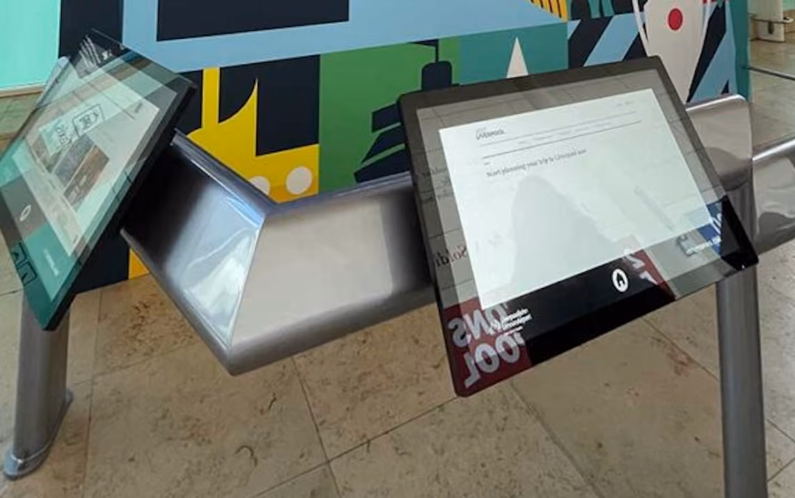 Angled flat-sided oval stainless steel tube used as an accessible interactive screen mount, mitre-cut and welded, with FSO leg supports.